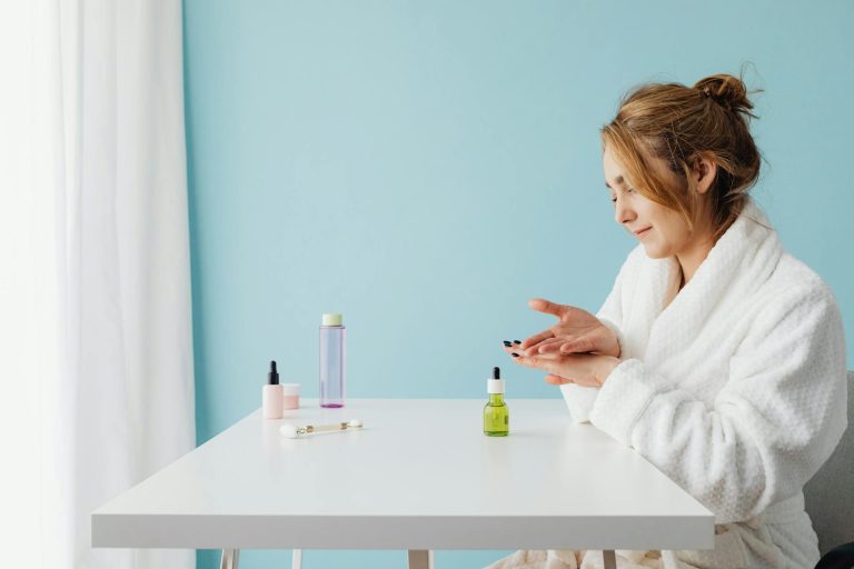 woman in a bathrobe sitting by a table and applying a product to her hands